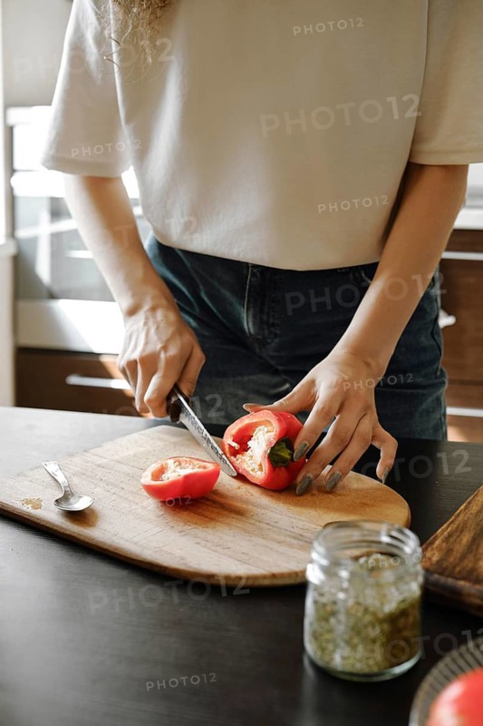 Unrecognizable woman cutting juicy bell pepper on a chopping board in the kitchen