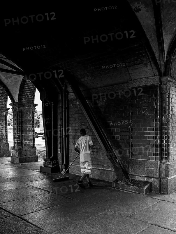 Black and white photograph, employee of the Berlin city cleaning service sweeping the pavement at the Oberbaum Bridge, Berlin, Germany