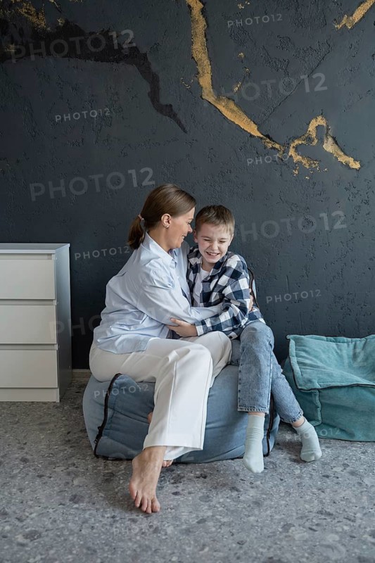 A mother and her son share a warm embrace while sitting on a comfortable bean bag in a stylish modern room. The moment captures love and family connection in a serene space