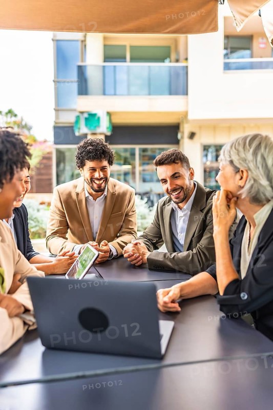Vertical photo of a group of diverse business people using laptop during a meeting in a cafeteria