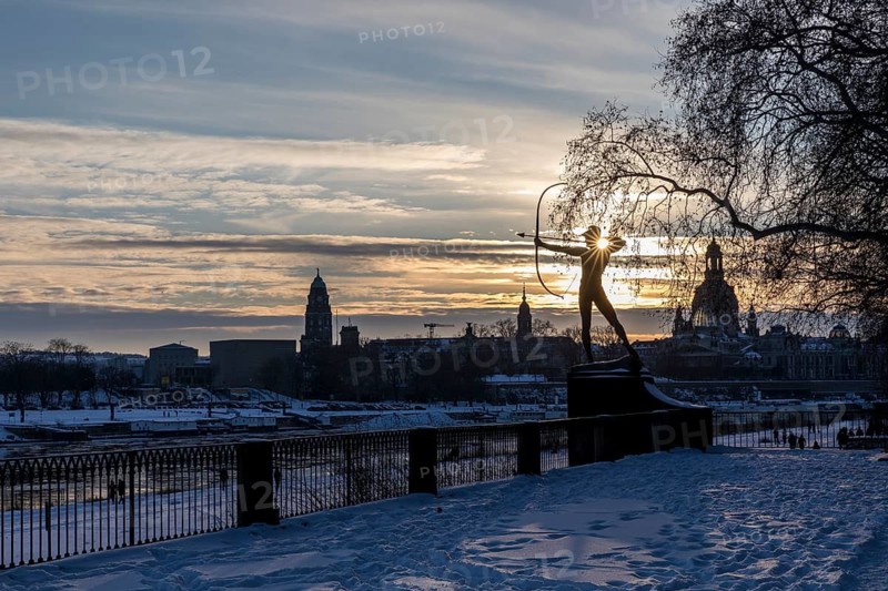 Bronze figure The archer in the snow, in the background the Elbe with drift ice and the old town with Church of Our Lady in the evening light, Dresden, Saxony, Germany