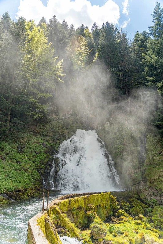 Stunning waterfall in Jaun, Gruyere region, Switzerland, showcasing the Gastlosen mountains. Spring view features intense mist and vibrant green foliage