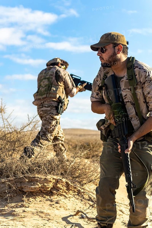 Two soldiers in camouflage gear navigate a sandy desert landscape, focused on a mission, with clear blue skies above. They are carrying weapons and wearing tactical equipment
