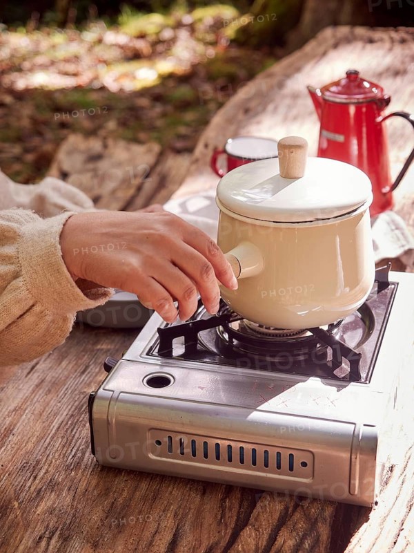Hand holding pot handle on gas portable stove on a wooden table, cooking outside