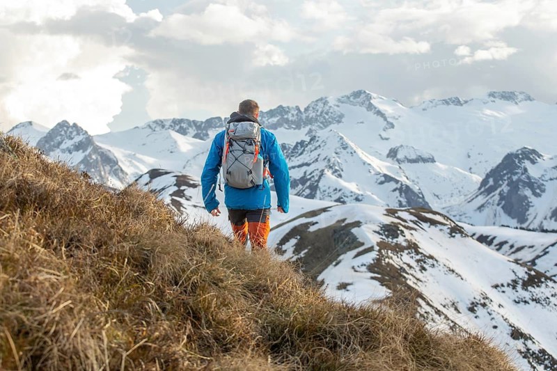 A man in outdoor gear treks along a scenic path in the Pyrenees mountains. Snow covered peaks create a breathtaking backdrop, capturing the spirit of adventure and exploration