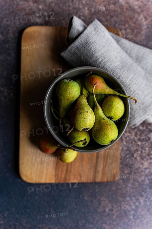 A top view of a bowl filled with fresh wild pears, resting on a wooden board. The rustic setting highlights the natural textures and vibrant green hues of the pears