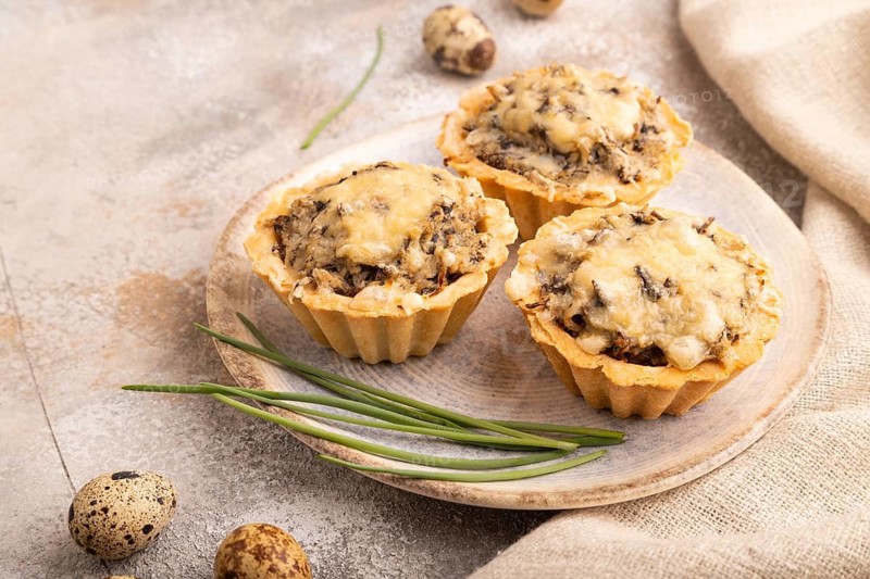 Tartlets with meat and cheese on brown concrete background and linen textile. side view, close up