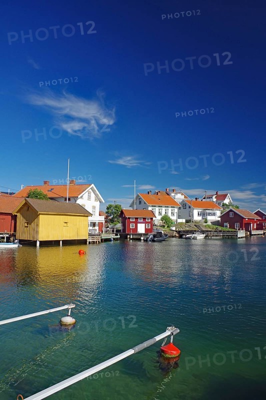 Coastal landscape with colourful wooden houses on an archipelago island by the water under a clear blue sky, Gullholmen, Västra Götalands län, Sweden