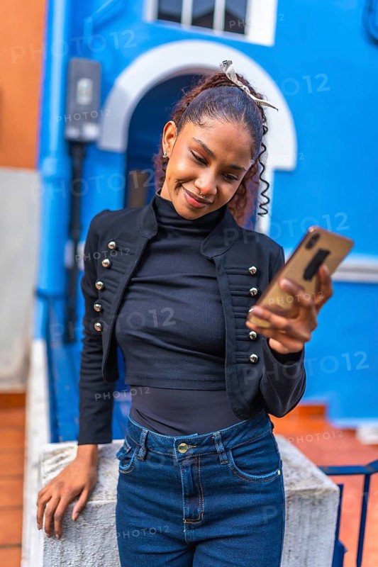 Beauty cool african american woman using smartphone leaning on a rail outside a blue vivid house