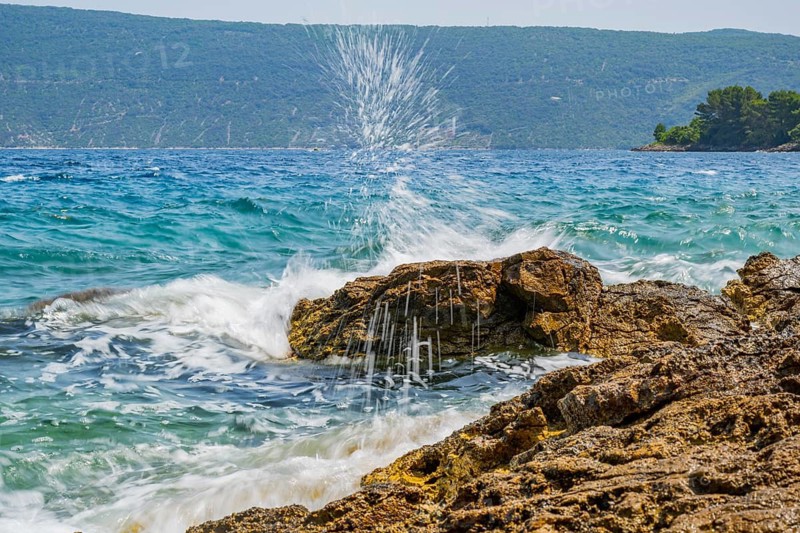 Wellen brechen an einem Felsen im Meer an einem sonnigen Tag auf der Insel Cres, Kroatien