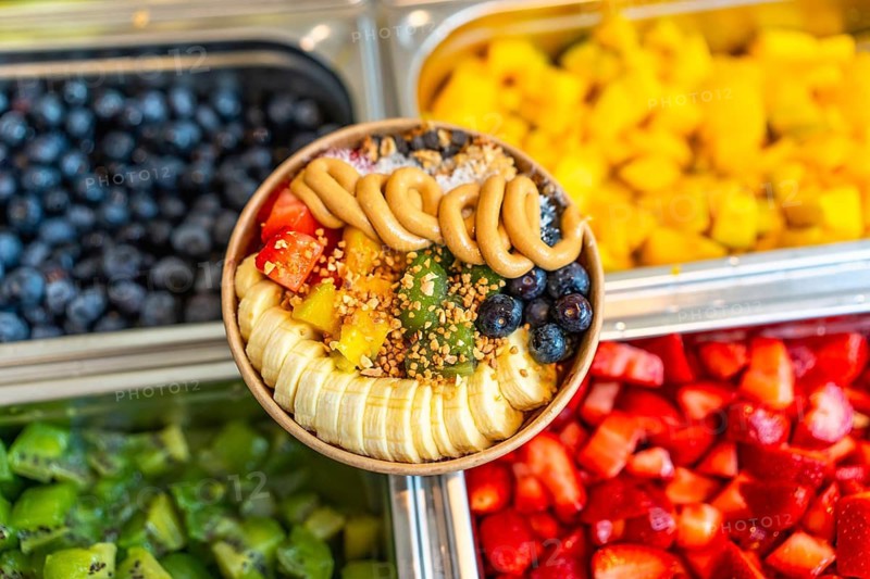Acai smoothie bowl with vibrant sliced banana, mango, kiwi, strawberries and blueberries, topped with peanut butter swirls, granola and bee pollen for a fresh, colorful breakfast bowl