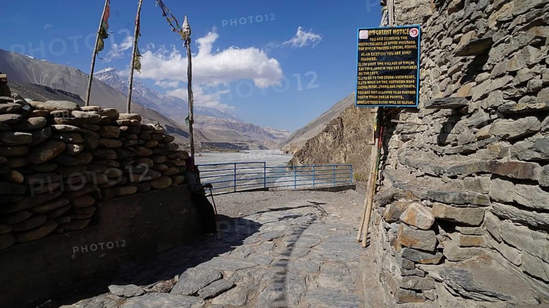 View of a rocky mountain road with a gate and sign to the entrance to the Upper Mustang region and a river in the background, trekking at Annapurna Circuit, Nepal