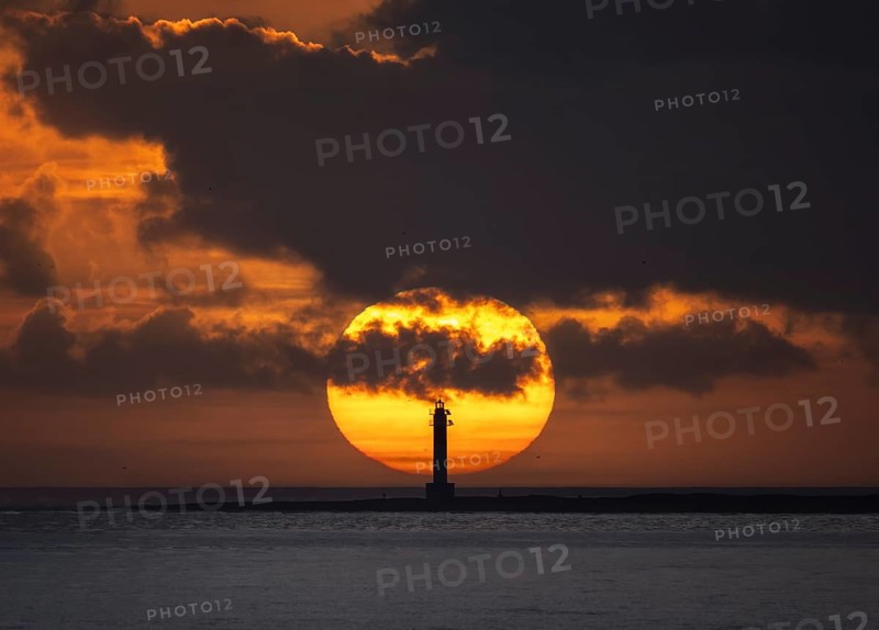 The silhouette of Fangar Lighthouse in Tarragona, Spain is captured against a dramatic sunset The striking colors and clouds create a breathtaking seascape