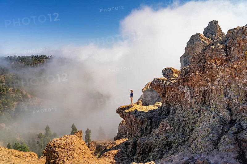 Distant unrecognizable person captured standing on a rugged cliff overlooking a misty landscape at Pico de las Nieves, Gran Canaria