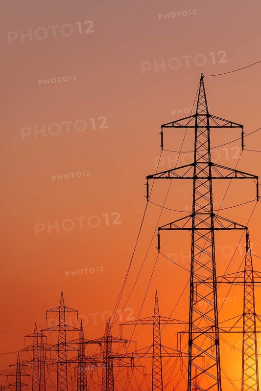 Silhouette of several high-voltage power lines and electricity pylons against a glowing orange and red sunset sky in Germany