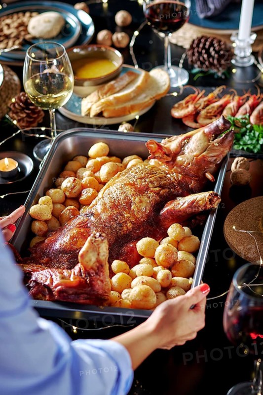 Cropped unrecognizable woman's hands serving in a sumptuously set dining table featuring a roasted suckling pig surrounded by potatoes, shrimp, wine, and bread, set in cozy candlelit ambiance