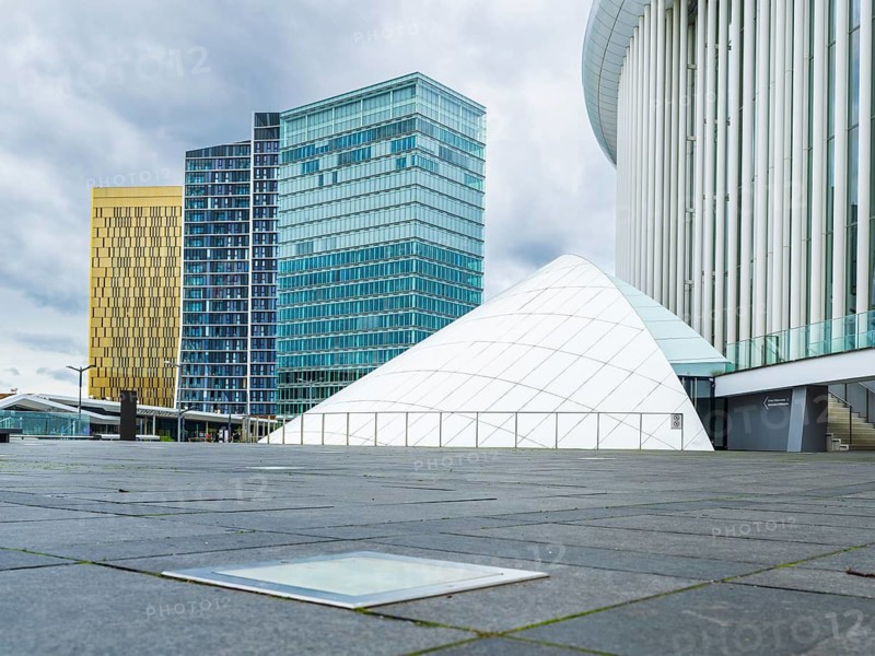 Exterior view of the Grande-Duchesse Joséphine-Charlotte Concert Hall on the Kirchberg Plateau in the European Quarter of Luxembourg City, Luxembourg, with surrounding modern high-rise office buildings. Contemporary architectural landmark photographed in daylight, featuring elegant columns, clean lines, and an urban business district atmosphere