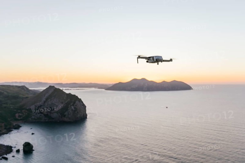 A drone gracefully flies over a tranquil coastal scene at sunset The tranquil ocean and silhouettes of distant islands create a peaceful backdrop of natural beauty