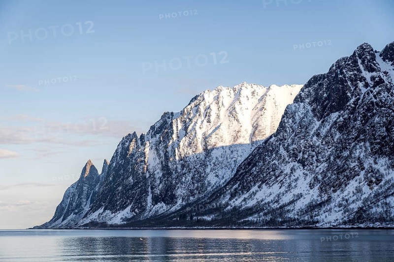 Spectacular view of snow-capped mountains reflecting in the clear blue waters of Ersfjord, Norway, capturing the serene beauty and dramatic landscape of the untouched wilderness