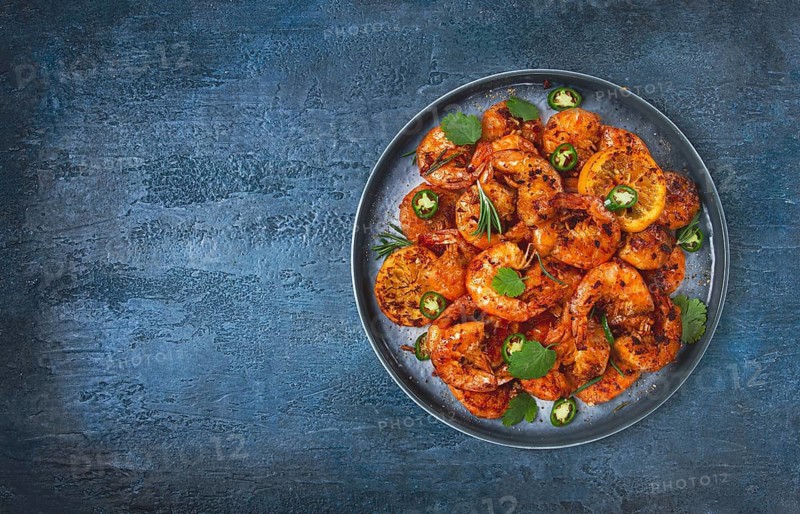 Grilled shrimp, unpeeled, headless, with spices, on a dark blue table, homemade, no people