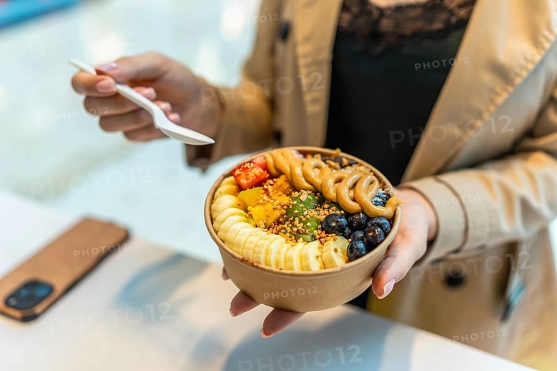 Woman holding a nutritious acai bowl filled with fresh fruit, granola, peanuts, and bee pollen, promoting a healthy lifestyle and mindful eating for breakfast or a snack