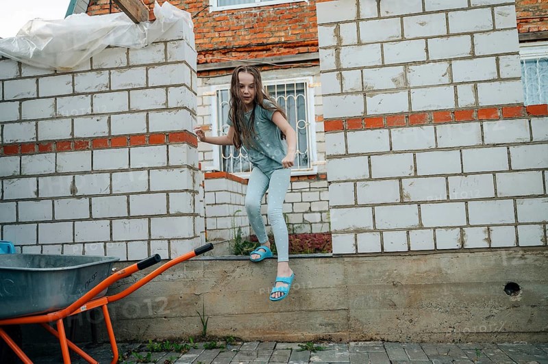 A young girl energetically plays and explores a construction site, demonstrating a sense of adventurous fun surrounded by unfinished brick structures and building materials