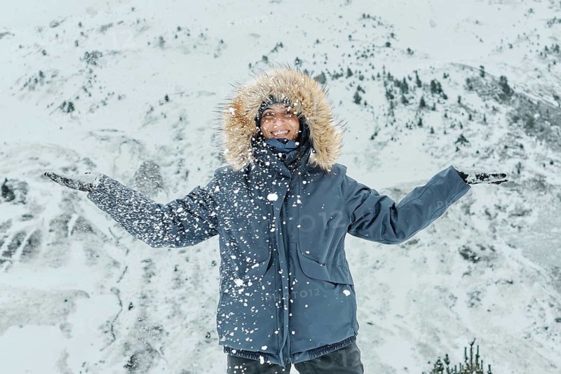 A woman, bundled in a fur-lined jacket, joyfully embraces the snowfall at Astun ski resort, nestled in the picturesque Huesca Pyrenees, capturing the essence of winter adventure