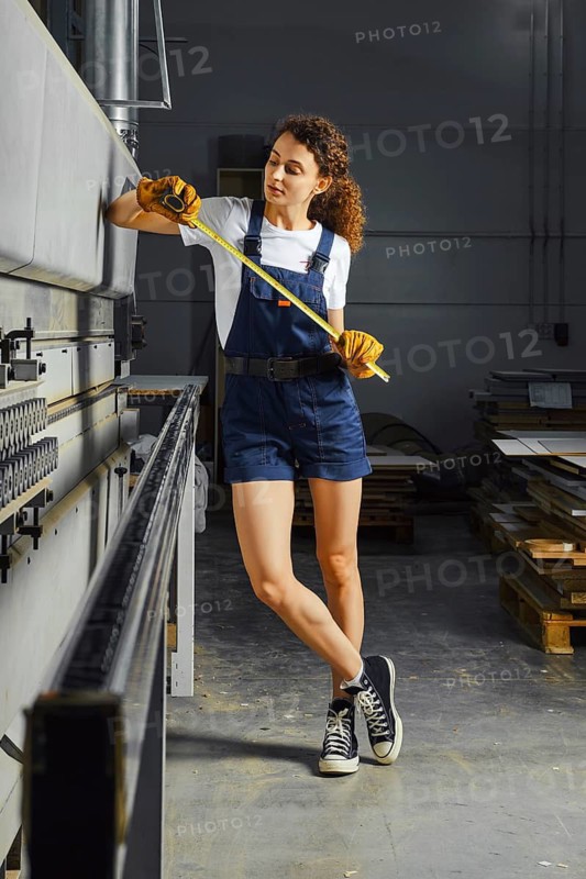Young woman near a woodworking machine with a steel tape measure in hand