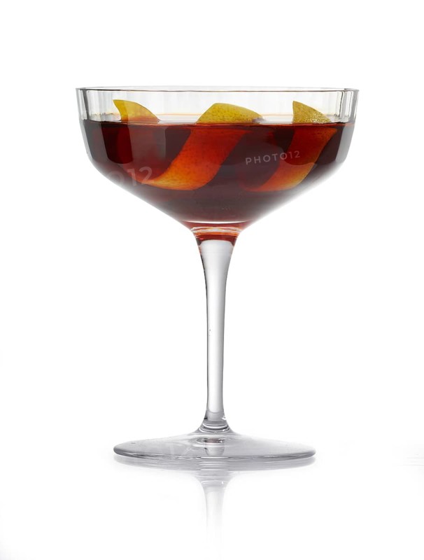 Cocktail in a coupette glass against a white background, a wide lemon zest as garnish, studio shot