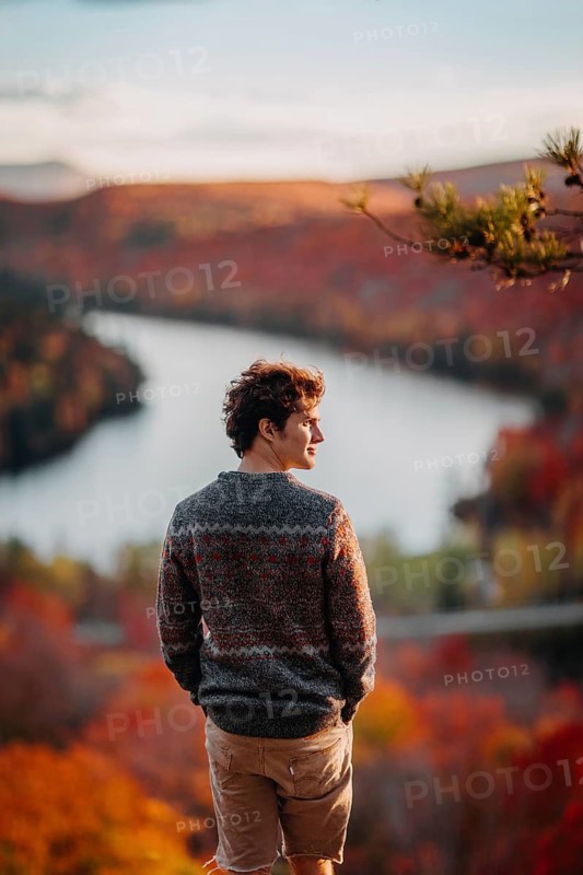 A man stands overlooking a vibrant autumn landscape in Quebec, Canada, as the foliage turns brilliant shades of red and orange, offering a breathtaking view of the season