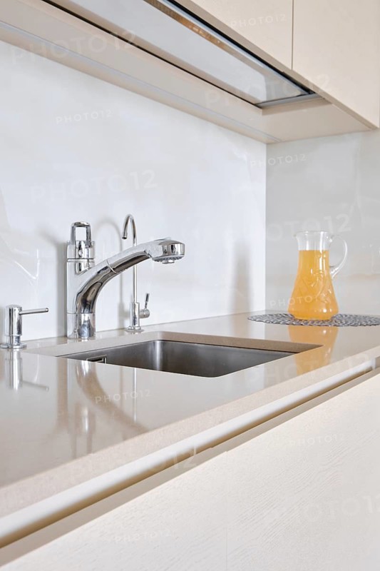 A bright and modern kitchen displays a stainless steel faucet and a clean sink. A pitcher of orange juice sits on a tasteful coaster beside the sink, enhancing the fresh ambiance of the space