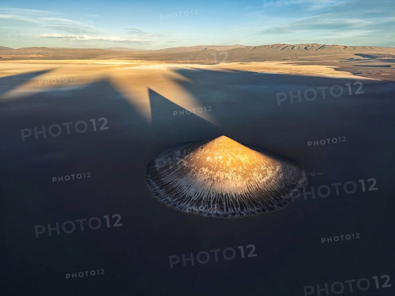 Top view, the stunning Cono de Arita rises dramatically from the salt flats of Salta, Argentina. This aerial shot captures the pyramid like shape bathed in the warm glow of sunrise, casting long shadows over the serene landscape