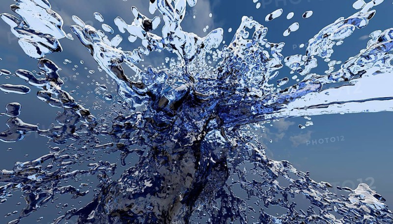 A captivating close-up of a dynamic water splash against a clear blue sky, capturing the fluid motion and shimmering details. Perfect for themes of nature and freshness