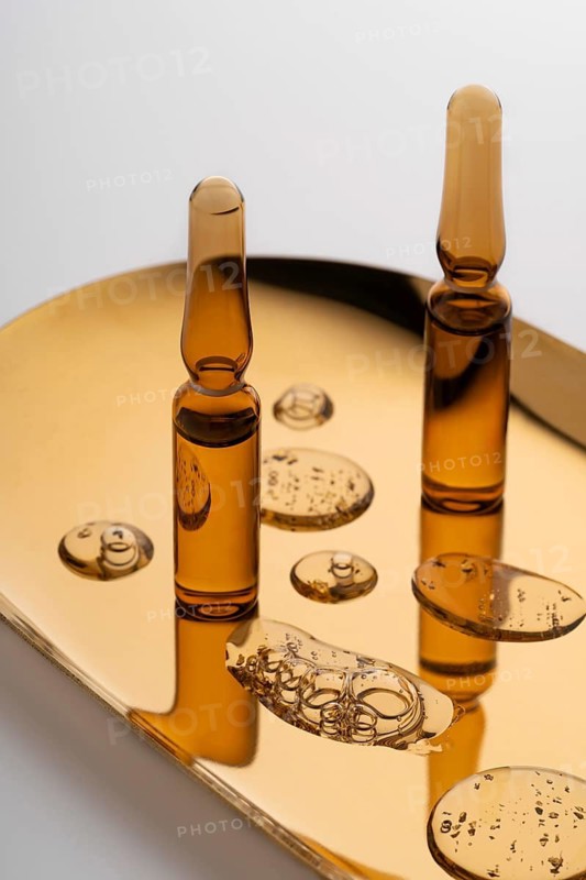 Elegant glass ampoules filled with potent anti-aging serum, showcased on a reflective golden surface, ideal for sophisticated skincare routines