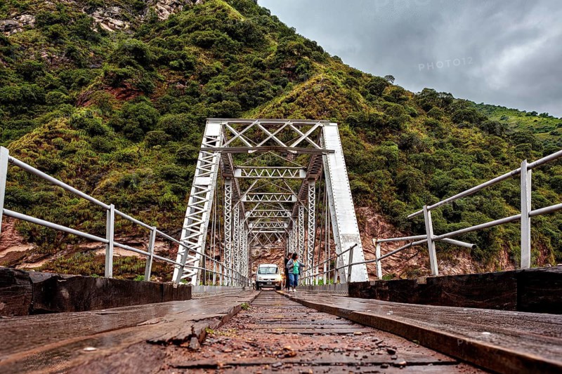 Metal bridge over a river against a backdrop of green mountains, roads through the Quebrada de Cafayate countryside near Salta in Argentina