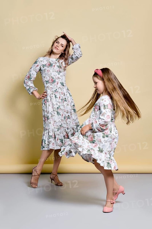 Beautiful mom and daughter in identical dresses dancing in studio