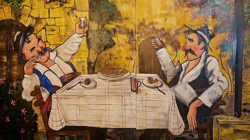 Humorous mural with two men dining at a table in a traditional village setting, Greek taverna by the Easter bonfire Psinthos, Holy Saturday, Easter, Psinthos, Rhodes, Dodecanese, Greek Islands, Greece