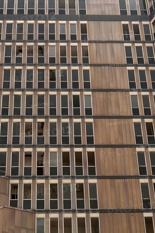 A pattern of windows of an abandoned high rise building, a dated architectural style with monochrome shades of grey and brown