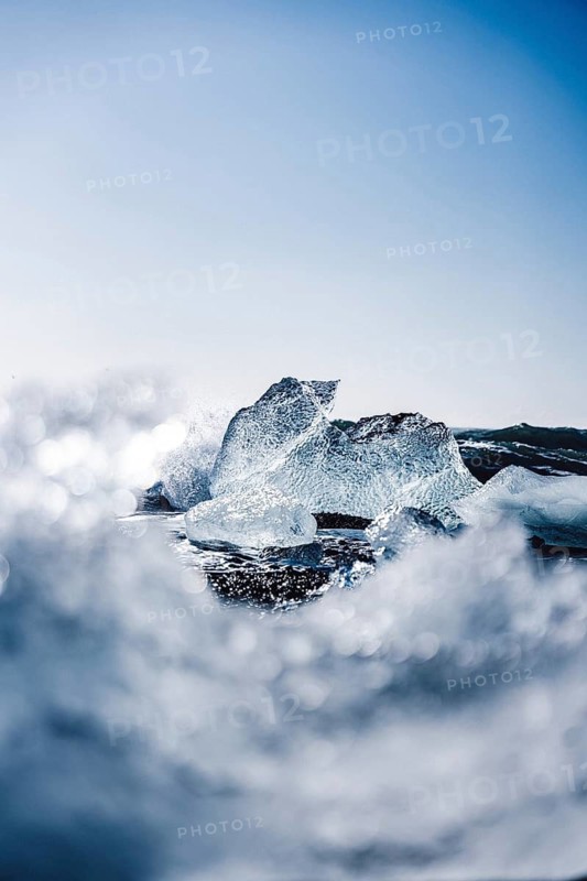 Captivating ice formations glisten in the sunlight on Diamond Beach, Iceland. The contrast of clear ice against the dark sand creates a stunning natural spectacle