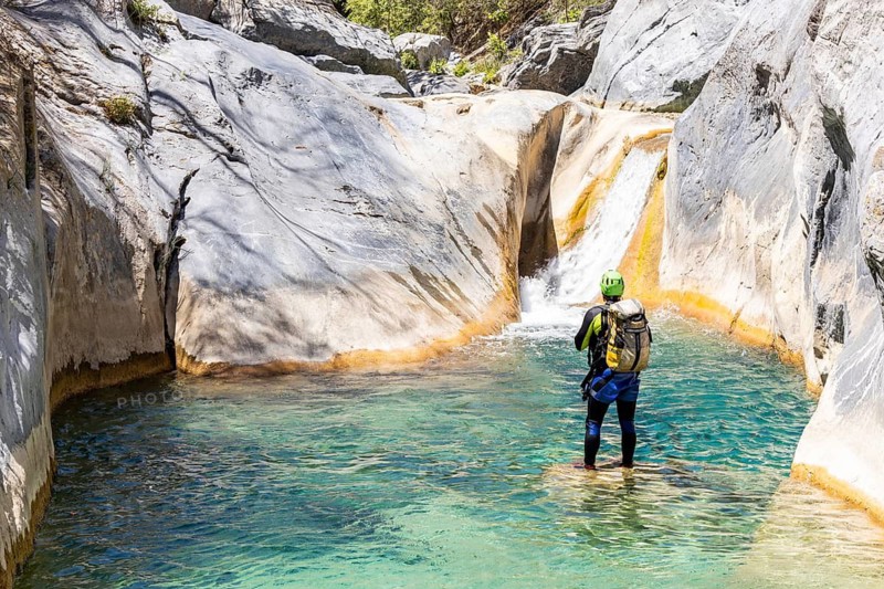 Back view of a canyoneer standing in a clear turquoise pool, preparing to climb a smooth natural slide among rocks in Matacanes, Nuevo Leon, Mexico. Adventure in nature