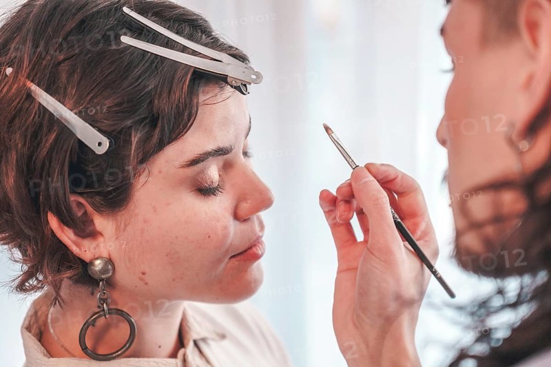 Professional makeup artist carefully applying makeup on a model's face using a brush, highlighting the skill and precision involved in creating a flawless look in a beauty salon environment