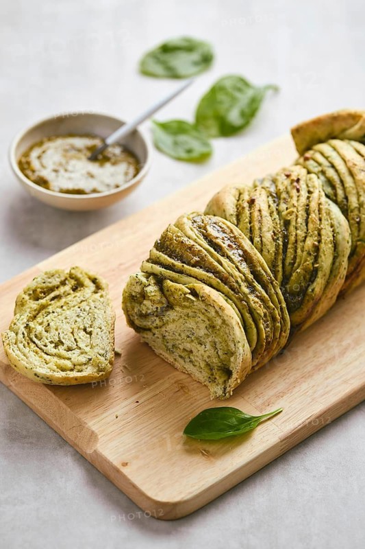 Baked homemade savoury babka plaited bread loaf flavoured with pesto on wooden bread board