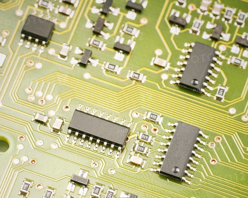 A detailed macro view of a green circuit board showing multiple black microchips and intricate gold pathways, representing technology, hardware, and electronics