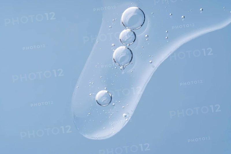 A close-up image of clear, transparent serum drops on a gentle blue background, capturing the light and purity of the liquid
