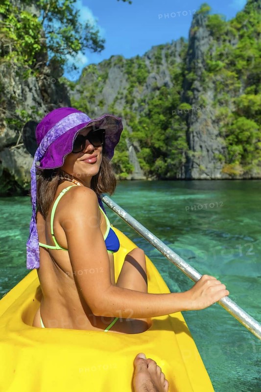 Young woman paddling a yellow kayak in the turquoise waters of twin lagoon, coron island, enjoying a sunny day in the philippines