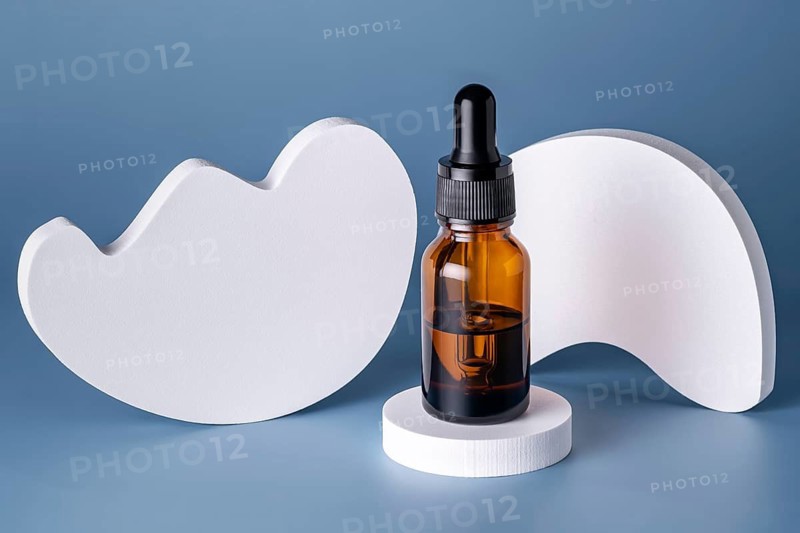 A single cosmetic serum bottle with a dropper, elegantly placed on a round white podium against a blue background, highlighted by abstract cloud shapes