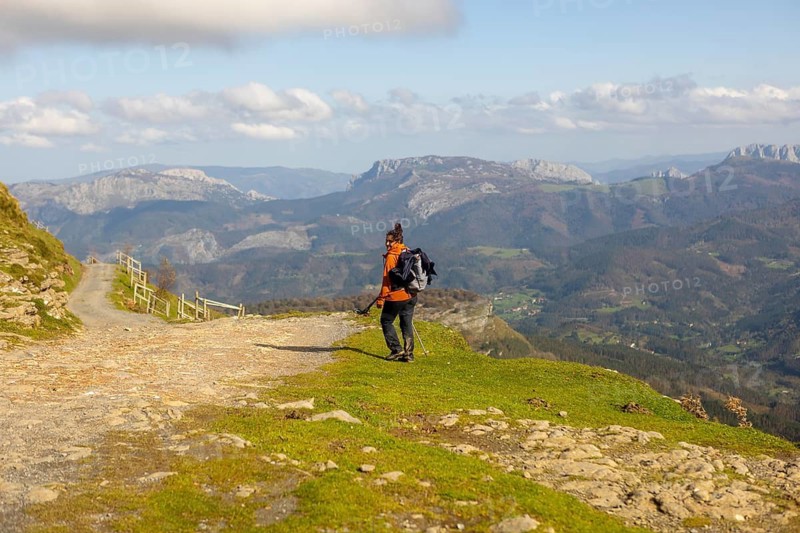 A woman enjoys a peaceful autumn hike in Gorbea Natural Park, Basque Country, Spain. Surrounded by stunning mountain views, she navigates the trails with a backpack and trekking poles