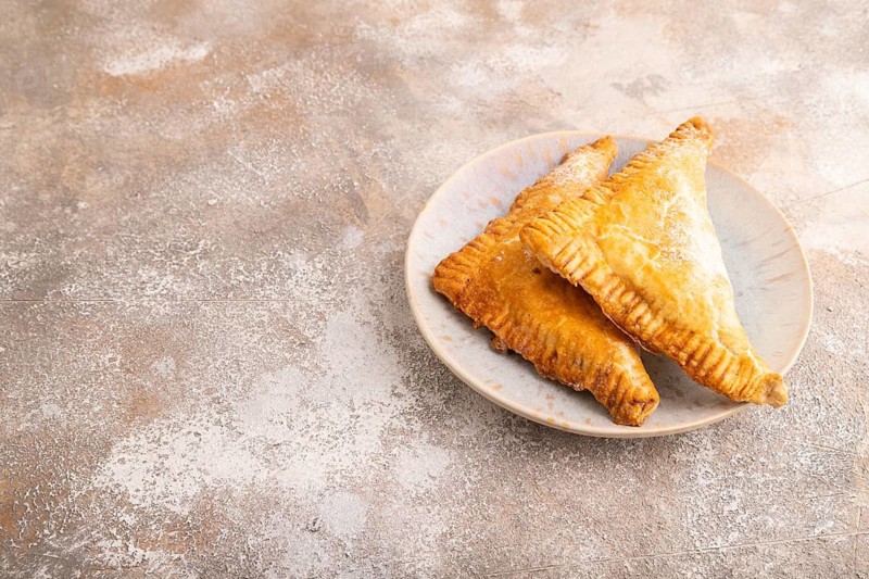 Triangles Pie, Puff Pastry, Samsa with cherry jam on brown concrete background, side view, copy space