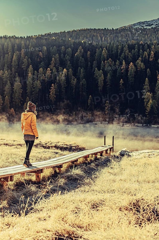 Young woman at Lake Staz near Sankt Moritz in the Engadine in Switzerland. Morning atmosphere with fog in autumn. Reflection of water