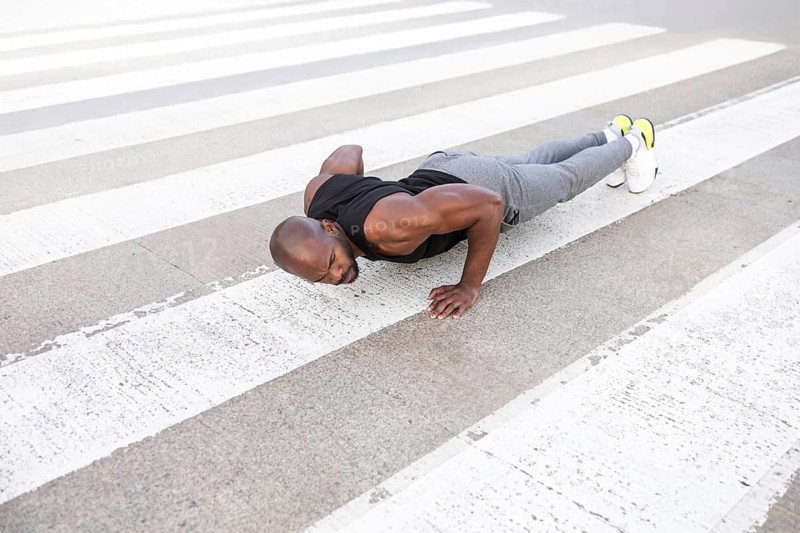 A fitness cuban man performs push ups on a city crosswalk, showcasing strength and dedication. Dressed in athletic gear, he exercises in an urban setting, embodying a healthy lifestyle